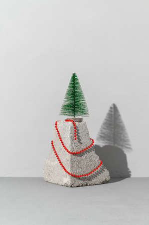 Conceptual festive card with trendy stone podium, miniature Christmas tree and red beads on gray background. Copy space, place for text, vertical orientation. Minimalist styleの写真素材