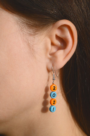 Handmade earring with number 2021 on the ear of a young woman. Close-up portrait, body part,...
