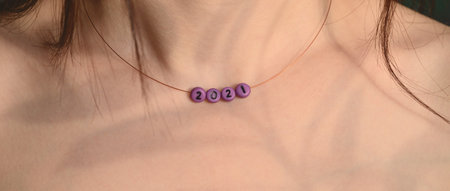 Handmade beads with number 2021 on the neck of a young woman. Close-up portrait, body part, selective focus. New Year's personal decorations. Copy space, shadow playの写真素材