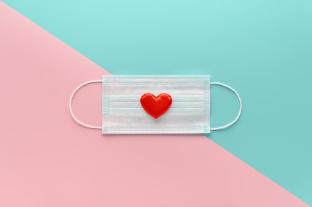 New normal Valentine's Day concept. Medical face mask decorated with red heart on pastel pink and cyan background. Top view, Copy Space, minimal composition. Creative flat layの写真素材