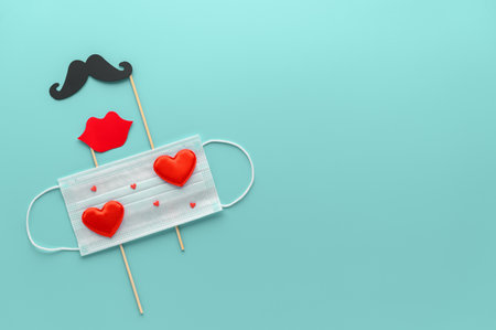New normal Valentine's Day concept. Medical face mask decorated with red hearts and paper mustache and lips on cyan background. Top view, Copy Space, minimal composition. Creative flat layの写真素材