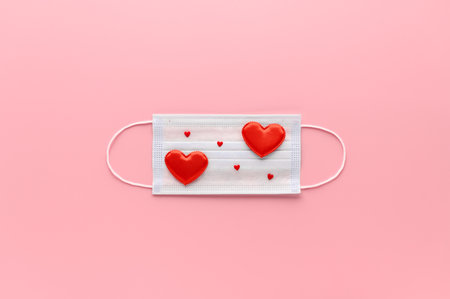 New normal Valentine's Day concept. Medical face mask decorated with red hearts on pastel pink background. Top view, Copy Space, minimal composition. Creative flat layの写真素材