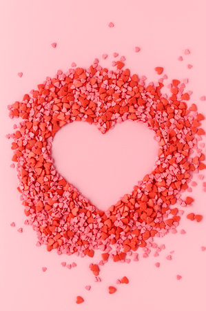 Valentine's day holiday greeting card. Heart-shaped confectionery sprinkling on pastel pink background. Flat lay, copy space, vertical orientationの写真素材