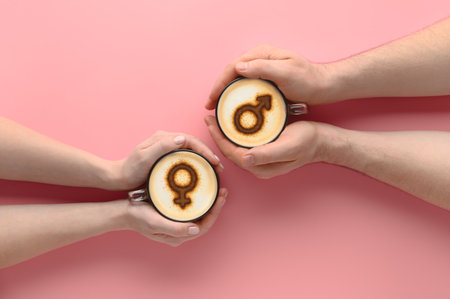 Top view Hands of couple in love holding cups of coffee with symbols of venus and mars on milk foam on pastel pink background. Concept romantic date on Valentine's day. Creative flat lay, copy spaceの写真素材