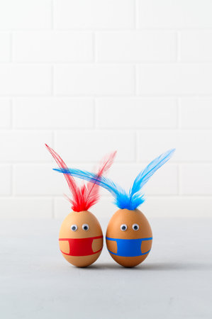 Coronavirus Easter concept. Two brown easter eggs wearing protection face mask and feather ears for Easter holidays decoration. Selective focus with copy spaceの写真素材