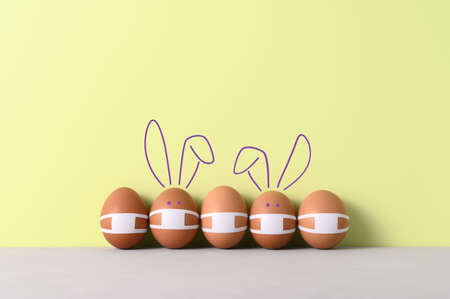 New normal Easter holiday concept. Easter eggs and cute bunnies wearing protective face masks in a...