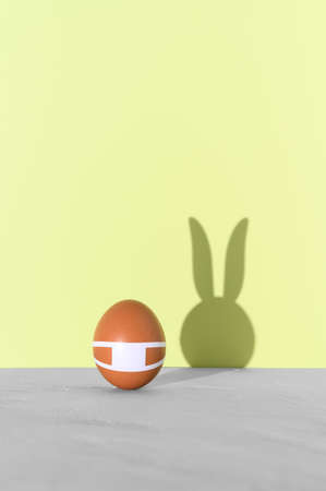 Easter minimal concept with egg wearing a protective face mask, and bunny ears shadow on the green backdrop. Creative funny holiday background. Copy spaceの写真素材