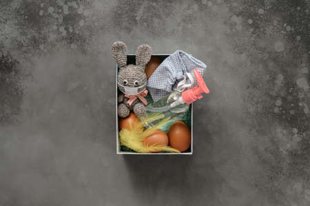 Packing homemade seasonal gift box or package for Easter Holiday. Eggs, protective face mask,...