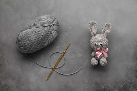Easter crafting DIY. Handmade crochet rabbit toy, ball of wool yarn, and knitting needle on dark gray background.の写真素材