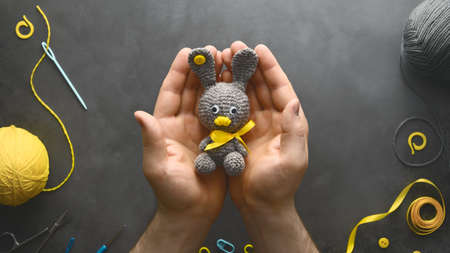 DIY Easter gift making theme. Human hands hold handmade knitted toy Easter rabbit and needlework...