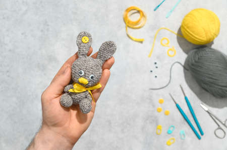 DIY Easter gift making theme. Human hands hold handmade knitted toy Easter rabbit and needlework...