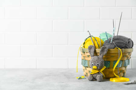 Easter crafting DIY. Handmade knitted toy Easter rabbit, and knitting accessories in the basket. White brick backdrop. Space for textの写真素材