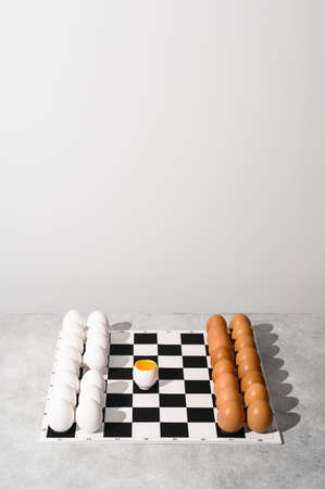 Chessboard with figures of white and brown eggs on a gray background. Creative Idea Easter and chess. Place for textの写真素材