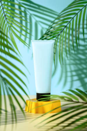 Ad template for sunscreen tube mock-up displayed on yellow podium on surrounded by palm leaves. Blue...
