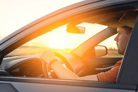 Caucasian Man in automobile in the countryside and sun rays. Male driver driving a car at sunset...
