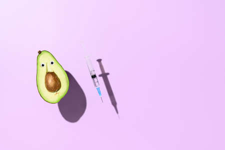 Concept of vaccination against virus. Half an avocado, syringe with vaccine against virus levitating over purple background. Minimalistic creative imageの写真素材