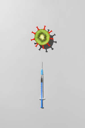 Concept of vaccination against coronavirus. Top view of syringe with vaccine against COVID-19 and half kiwi fruit in the form of virus on gray backgroundの写真素材