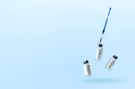 Concept of vaccination against coronavirus. Three vial with vaccine against COVID-19 and medical syringe, levitating over blue background. Minimalistic creative image with place for textの写真素材