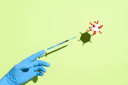 Coronavirus vaccination creative concept. Hand in medical glove, syringe with vaccine against...