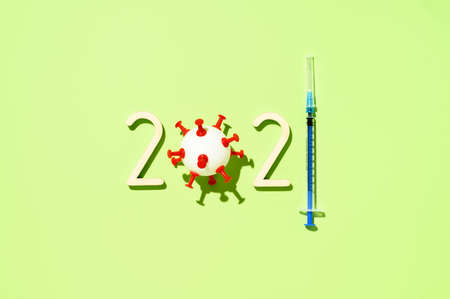2021 - year of mass vaccination against COVID-19 of the world population, the concept of victory over coronavirus. Overhead view of number 2021, syringe, and ball in form virus on pastel green backgroundの写真素材