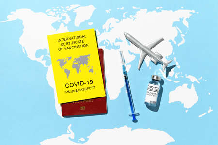 Traveling Immune passport, as proof vaccinated against Covid-19. Yellow Certificate of Vaccination, syringe, vial with vaccine, and toy plane on world map background. Top viewの写真素材