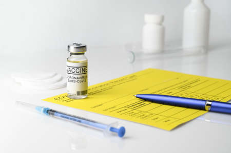 Coronavirus vaccination theme. Yellow vaccination record card, blue pen, a vial with covid-19...