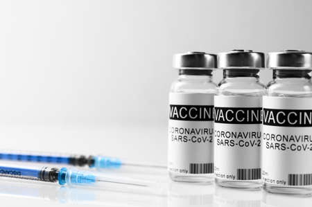 Coronavirus vaccination theme. Three vials with COVID-19 vaccine and syringes on glass laboratory white bench, close up, space for textの写真素材