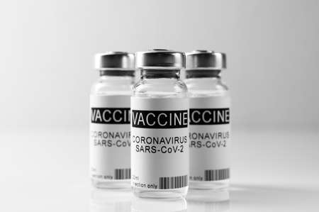 Coronavirus vaccination theme. Three glass vials with COVID-19 vaccine on white laboratory bench,...