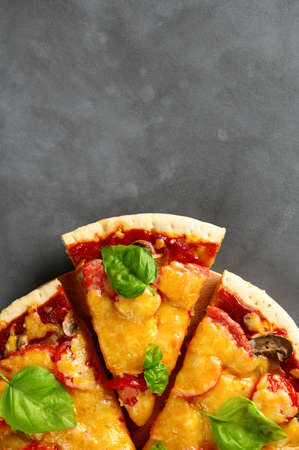 Top view of hot tasty homemade pizza with green basil leaves on the dark grey concrete background. Italian pizza on the black slate tabletop. With copy space for text. Flat lay, close-upの写真素材