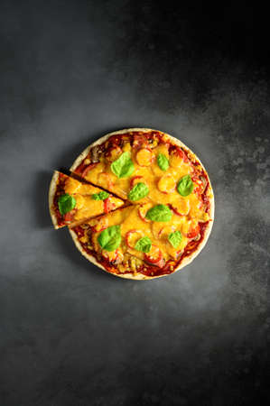 Top view of hot tasty homemade pizza with green basil leaves on the dark grey concrete background. Italian pizza on the black slate tabletop. With copy space for text. Flat layの写真素材