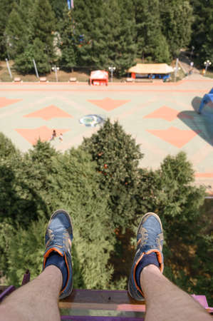 From above anonymous man in sneakers riding modern Ferris wheel over green trees on fairground in summerの写真素材