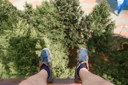 From above anonymous man in sneakers riding modern Ferris wheel over green trees on fairground in summerの写真素材