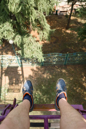 From above anonymous man in sneakers riding modern Ferris wheel over green trees on fairground in summerの写真素材