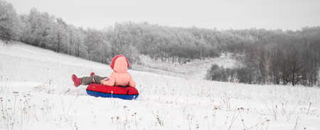Child girl is riding an inflatable sleigh from the hill. Outdoor activity recreation. Open-air living and Scandinavian concept: Fruitsliv.の写真素材