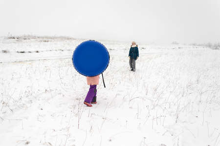 Sisters is riding an inflatable sleigh from the hill. Outdoor activity recreation. Open-air living and Scandinavian concept: Fruitsliv.の写真素材