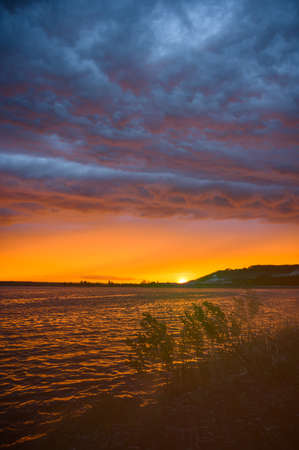 Thunderstorm sky over lake at sunset. Bright sunburst over the lake.の写真素材