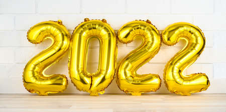 Gold helium balloons numerals 2022 on white brick wall background. Happy new year 2022 concept. Greeting and invitation cardの写真素材