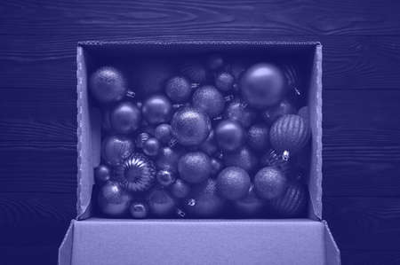 Overhead view of many Christmas balls in a cardboard box on a dark wooden background. Toned in trendy Very Peri Color Of The Year 2022.の写真素材