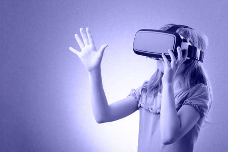 Little girl playing in virtual goggles indoors. Metaverse concept. Toned in trendy Color Of The Year 2022 - Very Peri.の写真素材