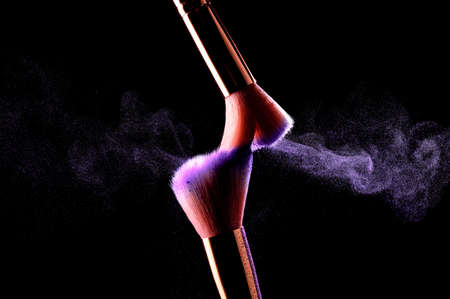 Make-up brushes with cosmetic powder explosion on black background. Skincare or fashion concept.の写真素材