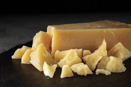 Authentic Italian Parmigiano Reggiano: Aged Cheese Slice on Black and Wooden Backgrounds.