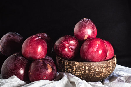Juicy Summer Plums: Fresh Red and Black Plums on a Rustic Wooden Background.の写真素材