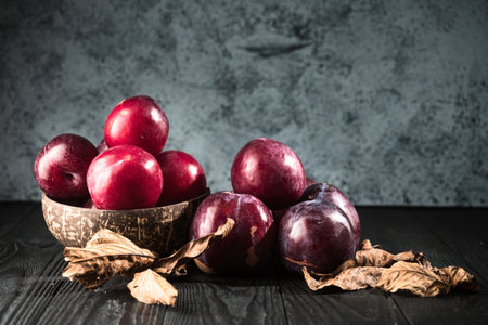 Juicy Summer Plums: Fresh Red and Black Plums on a Rustic Wooden Background.