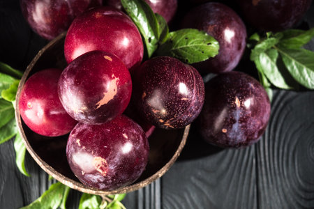 Juicy Summer Plums: Fresh Red and Black Plums on a Rustic Wooden Background.の写真素材