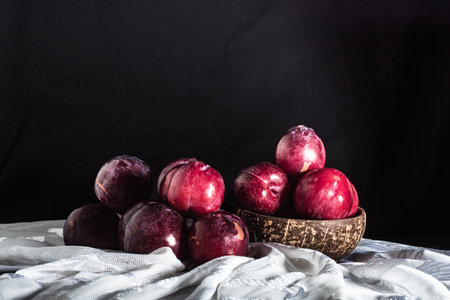 Juicy Summer Plums: Fresh Red and Black Plums on a Rustic Wooden Background.の写真素材