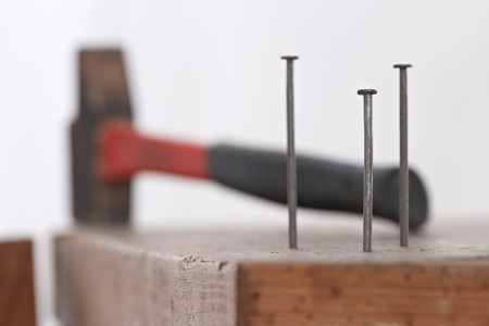 close up of nails planted in a wooden cabinet with a hammer to tinkerの写真素材