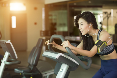 Happy woman riding an exercise bike in gymの写真素材