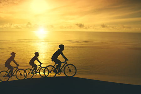Empty Copy Space Sporty company friends on bicycles outdoors against sunset Silhouette five 3 cyclist going along shoreline coast Reflection sun on water Sport in Nature background Group of peopleの写真素材