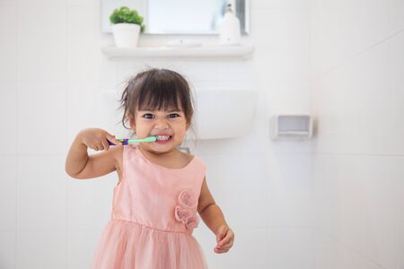 Little cute baby girl cleaning her teeth with toothbrush in the bathroomの写真素材