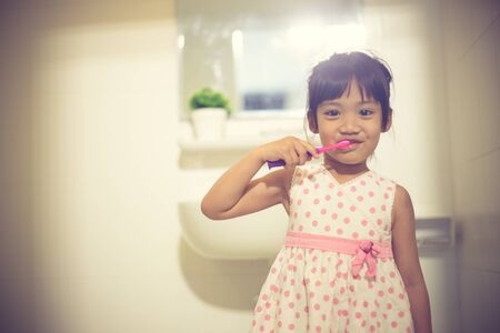 Little cute baby girl cleaning her teeth with toothbrush in the bathroomの写真素材